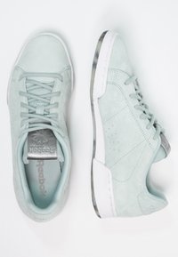 Ljusmintgröna mockasneakers med vita gummisulor. Inkluderar snörning, texturerade detaljer och metalliskt logo på plösen.