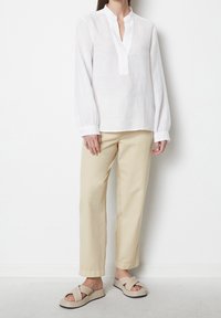 Blouse en lin blanc avec un col mandarin et des manches longues, associée à un pantalon en coton beige et des sandales à plateforme beige clair.