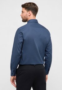 Camicia blu navy con bottoni, piccoli pois bianchi, maniche lunghe e colletto strutturato. Presenta un taglio dritto e polsini con bottoni.