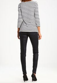 Svartvit randig långärmad tröja med rund halsringning, i kombination med svarta tighta jeans och svarta högklackade skor.