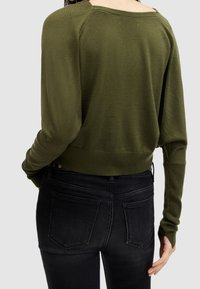 Maglione verde oliva con scollo ampio, maniche lunghe e orlo a coste. Abbinato a jeans neri con tasche posteriori classiche.