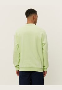 Sudadera verde claro con cuello redondo y puños acanalados, hecha de una tela suave, con un corte relajado y detalles de costura mínimos.