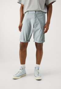 Pantalones cortos de algodón de color azul claro con dobladillo doblado, frente plano y cierre de botón, combinados con zapatillas altas de color azul claro y calcetines blancos.