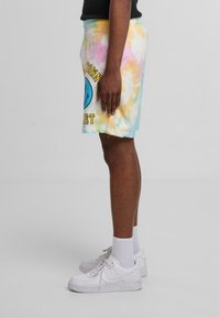 Tie-dye shorts i pastelfarver med et blåt smiley-ansigt grafik og tekst, parret med hvide sneakers og crew-sokker.
