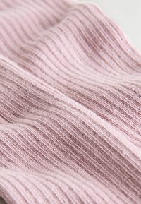 Weicher, gerippter rosa Strickstoff mit sichtbarer Textur und sanften Falten, die ein wellenförmiges Muster bilden.