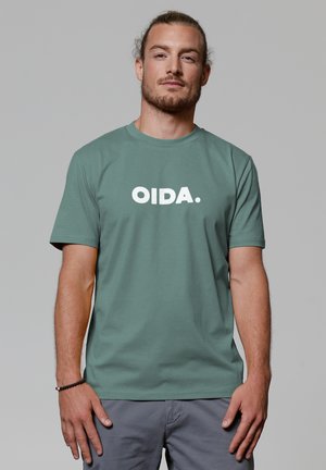 Muntgroen t-shirt met korte mouwen en een witte tekstafbeelding met de tekst "OIDA." Ronde hals, gemaakt van katoen, met een losse pasvorm.