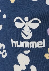 Granatowa tkanina o teksturowanym wzorze z białymi i pastelowymi abstrakcyjnymi kształtami. Na tle tkaniny widnieje wyraźne białe logo z napisem "hummel".