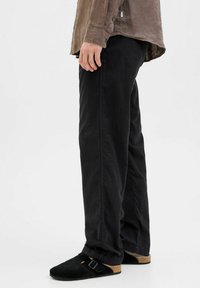 Black, loose-fitting trousers made of cotton, featuring a straight-leg design and a smooth texture. Accompanied by black suede clogs with buckles.