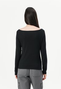 Top nero a maniche lunghe con un'ampia scollatura a spalle scoperte. Realizzato in tessuto liscio, presenta maniche aderenti e un orlo leggermente curvato.