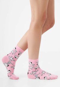 Rosa Knöchelsocken mit einem Muster von Cartoon-Hunden in Schwarz und Weiß. Die Socken haben einen gerippten Bund und eine glatte Stricktextur.
