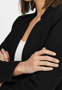 Černý texturovaný blejzr s moderním otevřeným střihem. Vyznačuje se subtilním vzorem a strukturálními rameny. Nosit se na bílé tričko.