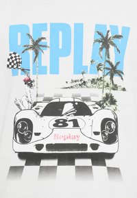 Λευκό μπλουζάκι με γραφικό ενός αγωνιστικού αυτοκινήτου με τον αριθμό "81", φοίνικες, μια σημαία καρώ και τη λέξη "REPLAY" σε μπλε χρώμα.