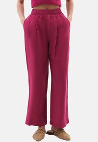 Fuksia laaja-housut korkealla joustavalla vyötäröllä, joissa on etupleitejä ja sivutaskuja. Yhdistetty teksturoituihin liukuvaan kengät.