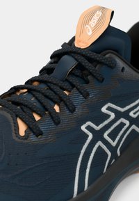 Baskets de sport bleues présentant un dessus texturé, des lacets noirs, des accents de logo blancs et une languette beige, conçues pour la performance et le confort.
