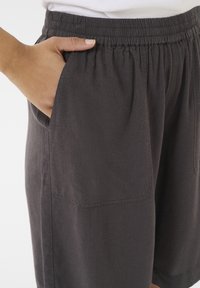 Pantaloni corti grigi, fino al ginocchio, realizzati in un tessuto leggero con cinturino elastico e tasche laterali, caratterizzati da una superficie liscia e un design minimale.