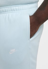 Pantalones de chándal Nike de color azul claro con una textura suave, que cuentan con un logo bordado en blanco en el muslo y una cinturilla elástica con bolsillos.
