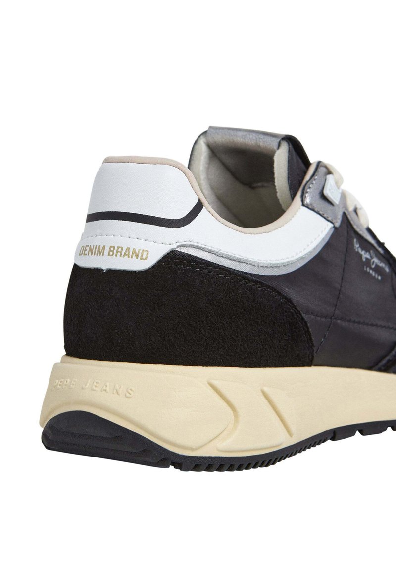 Zapatillas en negro y azul marino con materiales de ante y textil, acentos blancos y una suela de goma color crema. Presenta "DENIM BRAND" grabado en el talón.