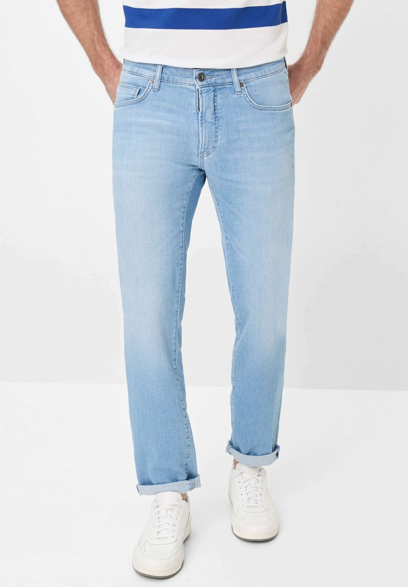 Jean en denim bleu clair avec une coupe droite, présentant des poches avant, un zip à boutons et des ourlets retournés. Porté avec des baskets blanches.