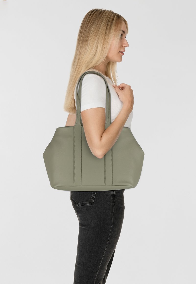 Borsa a tracolla verde in pelle sintetica con accenti cuciti, manici larghi e apertura superiore, tenuta da una persona di profilo su uno sfondo neutro.