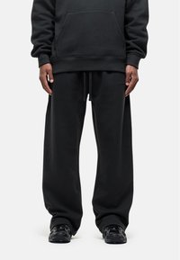 Zwarte sweatshirt en bijpassende sweatpants in een relaxte pasvorm, met een voorzak, een verstelbare tailleband en textiel met structuur. Zwarte sneakers.