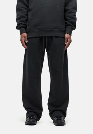 Zwarte sweatshirt en bijpassende sweatpants in een relaxte pasvorm, met een voorzak, een verstelbare tailleband en textiel met structuur. Zwarte sneakers.