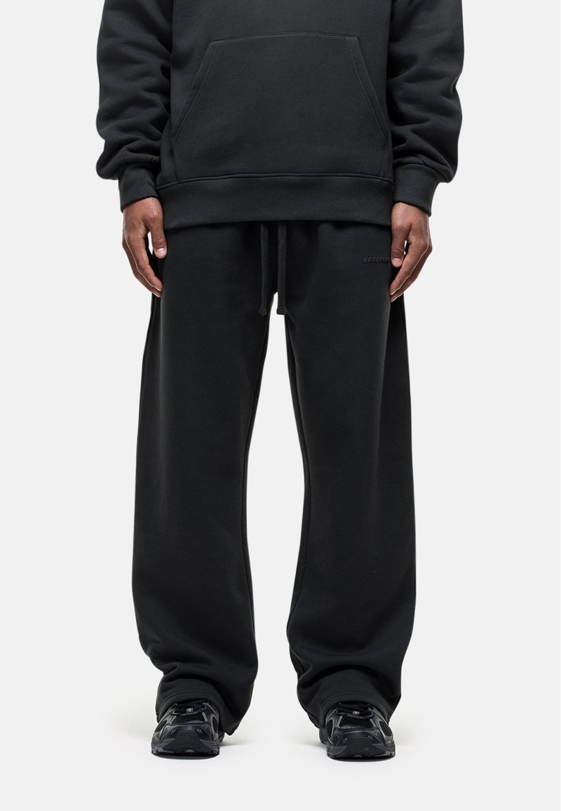 Zwarte sweatshirt en bijpassende sweatpants in een relaxte pasvorm, met een voorzak, een verstelbare tailleband en textiel met structuur. Zwarte sneakers.