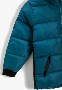 Teal pufferjack met een rits aan de voorkant. Heeft een capuchon, elastische manchetten en zijzakken. Gladde, glanzende stof met een gewatteerd patroon.