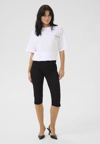 Biele skrátené tričko s krátkymi rukávmi, s potlačou. Čierne capri nohavice so slim fit. Čierne lodičky na vysokom podpätku.