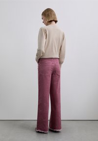 Pull-over beige en maille avec manches bouffantes, associé à un jean large rose à motif zèbre, avec des ourlets effilochés.