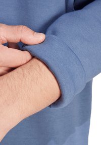 Felpa blu a maniche lunghe con una texture morbida, che mostra un risvolto tenuto da una mano, caratterizzata da una finitura del tessuto liscia e uniforme.