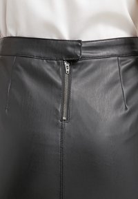 Černá kožená sukně s hladkým povrchem, vysokým pasem, zapínáním na zip na zadní straně a prošívanými detaily podél švů.