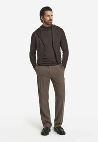 Ciemnobrązowy lekki sweter z kapturem, noszony na dopasowanym golfie. W zestawie z beżowymi spodniami w kratę i czarnymi mokasynami.