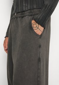 Dunkelgraue Hose mit lockerer Passform, elastischem Bund, seitlicher Tasche und gerippten Akzenten am Bund und der Taschenöffnung.