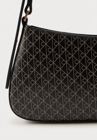 Μαύρη τσάντα χειρός με υφή, που διαθέτει ένα αλληλένδετο σχέδιο σε καφέ απόχρωση. Έχει κυρτό σχήμα και λεπτό λουράκι ώμου.