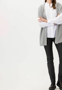 Cardigan gris claro sobre una camisa blanca de botones, combinado con pantalones negros y zapatos negros. El cardigan tiene un corte relajado y un frente abierto.
