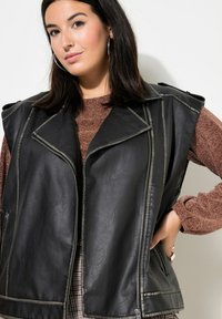 Schwarze Lederweste mit Motorraddesign, ausgestattet mit einem Reißverschluss und großen Klappen. Texturierte Oberfläche mit kontrastierenden Stichdetails.