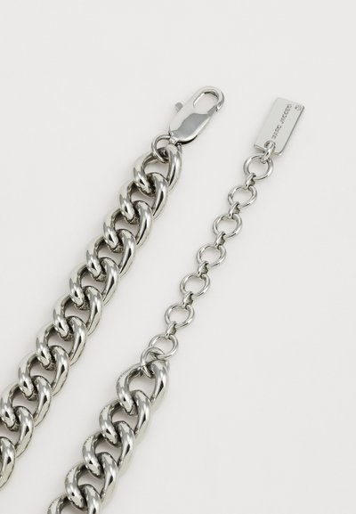 Kraftig silvrig kedjearmband med en krabba stängning och en justerbar tunn kedja som avslutas med en liten rektangulär graverad tag.
