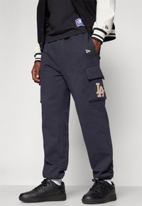 Marina cargobyxor i mjukt tyg har sidofickor och en ljusbrun broderad "LA"-logotyp. Matchas med svarta sneakers och en mörk t-shirt.