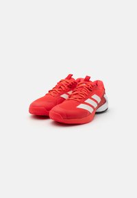 Red athletic shoes with a mesh upper, featuring white stripes, a padded collar, and a textured rubber sole for traction.