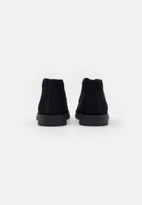 Bottines en nubuck noir avec une texture lisse, un bout arrondi et des semelles en caoutchouc. Design minimaliste sans matériel ou accents visibles.