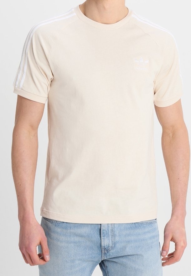 Beige bomullströja med korta ärmar, rundad halsringning och vita accentstripes på axlarna. Har en liten logotyp på bröstet.