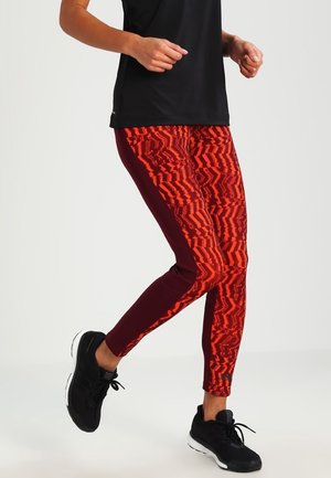 Leggings de sport en un motif zigzag vibrant rouge et orange, avec une coupe ajustée, des panneaux latéraux bourgogne profonds et une longueur cheville.