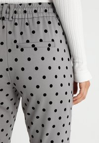 Grijze broek met stippen in zwart, voorzien van een elastische tailleband en een achterzak. Het materiaal lijkt glad met een casual ontwerp.