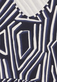 Granatowy materiał z odważnymi, białymi, geometrycznymi paskami o różnych szerokościach i kątach, z dekoltem w kształcie litery V i detalem zgromadzonego hemu.