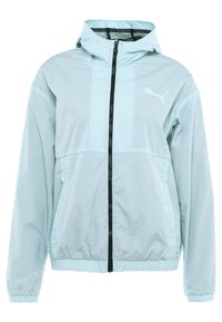 Ljusblå vindjacka med huva, svart dragkedja, elastiska manschetter och en vit Puma-logotyp på bröstet. Har en slät, lätt textur.