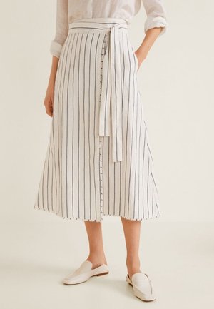 Hvidstribet linnednederdel med omslagsdesign, bånd til at binde, knaplukning og frynset kant. Kombineret med hvide slip-on sko.