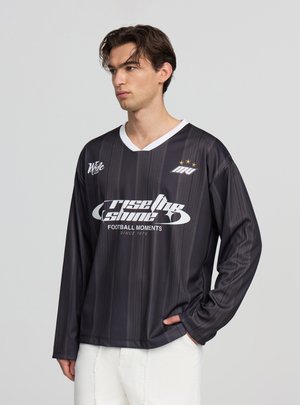 Maglia da calcio nera a maniche lunghe con strisce verticali, scollo a V bianco e testo grafico bianco audace. Tre stelle sopra il logo.