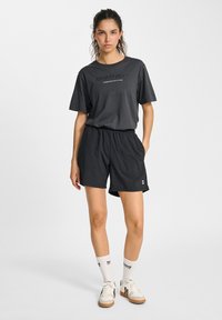 Svart kortärmad t-shirt med texten "SPORTS DEPT" och svarta träningsshorts. Vita sportstrumpor och beige sneakers fulländar looken.