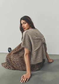 Beige neulotut lyhythihaiset neuleet, joissa on takaosan nauhakiinnitys, yhdistettynä ruskeaan leopardikuvioiseen hameeseen. Sujuva kangas, joka on rentoa mitoitusta.