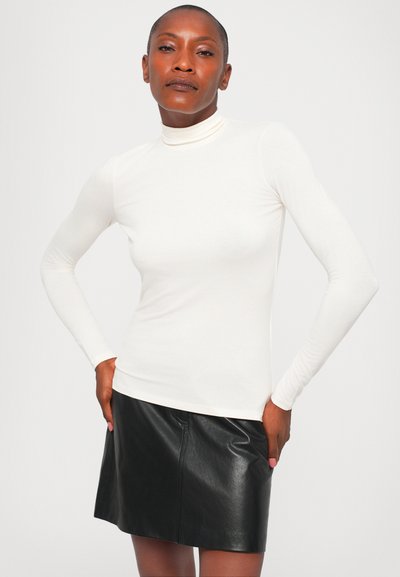 Bijeli dugi rukav turtleneck top napravljen od mekanog materijala, u kombinaciji s crnom kožnom mini suknjom koja ima glatku teksturu i uski kroj.